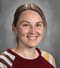 headshot - smiling female teacher with dirty blonde hair pulled back in the ponytail with a raglan sleeved shirt that's maroon with striped sleeves