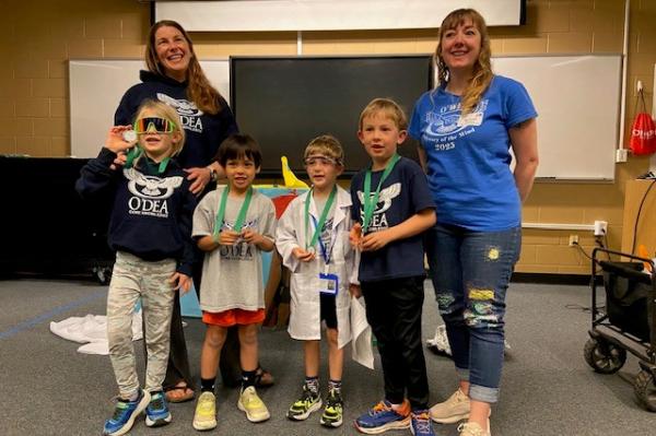 primary boys standing beside each other between two coaches (moms) posing for their photo at the Odyssey of the Mind competition 