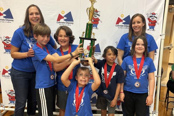 two mothers, bookcasing five very excited children - four boys and one girl - holding their 2nd place trophy for winning 2nd place at the odyssey of the Mind State tournament