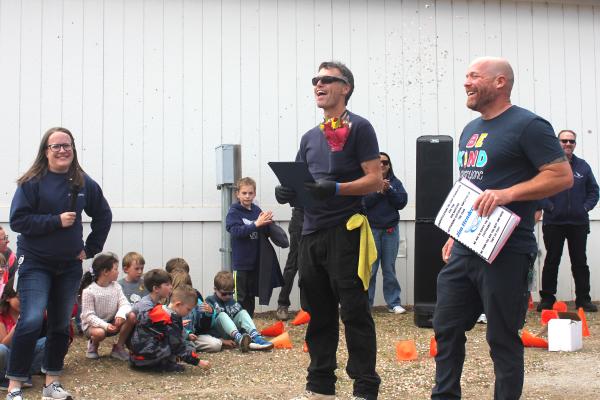 woman with award, male custodian smiling, male principal smiling holding papers outside award ceremony, few students in the background