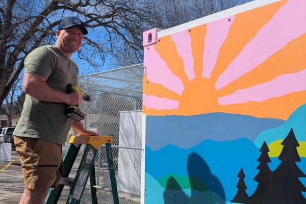 man on a ladder with a power drill attaching mural to a shipping container