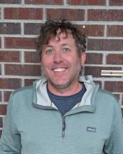 Koz standing up against a brick wall smiling