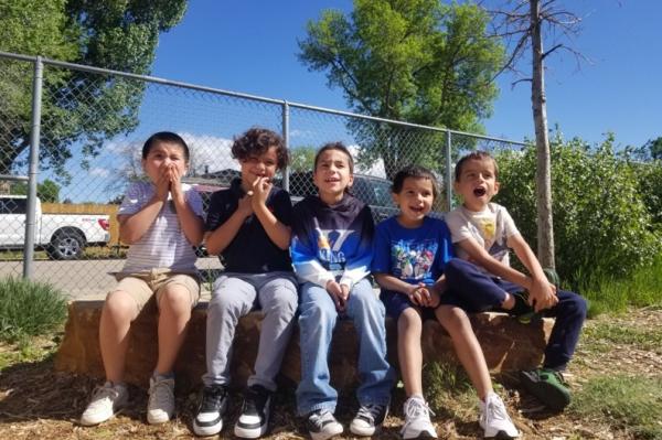 five boys sitting on a rock smiling and laughing at recess