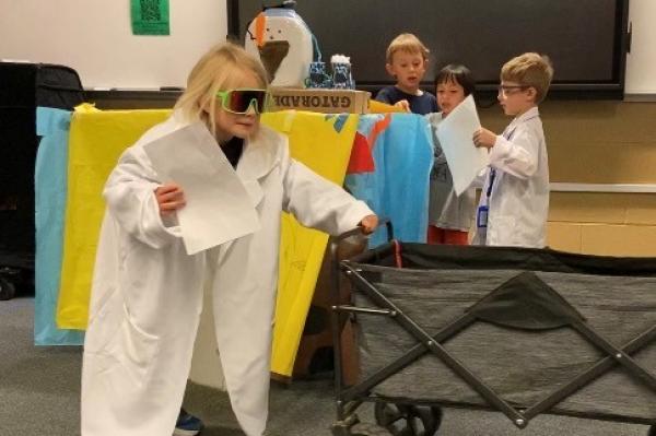 four primary age boys presenting a skit in Odyssey of the Mind, two in white scientists coats the others reading a script 