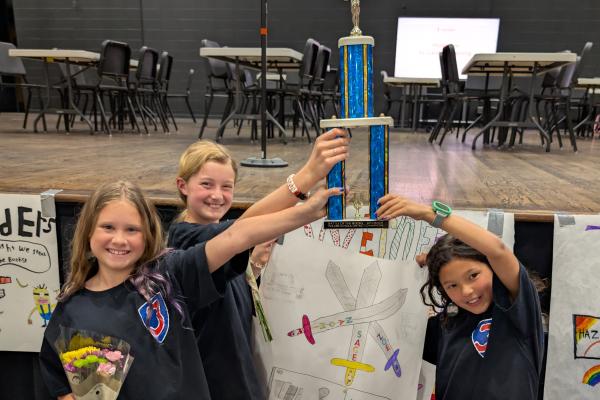 three girls smiling holding a battle of the books district 4th grade trophy
