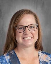 headshot - smiling teacher with reddish brown long hair with glasses and a blue flowered print top