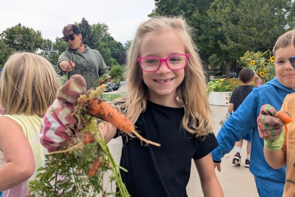Girl holding a carrot pulled from O'Dea garden clubs planters with a big smile on her face.