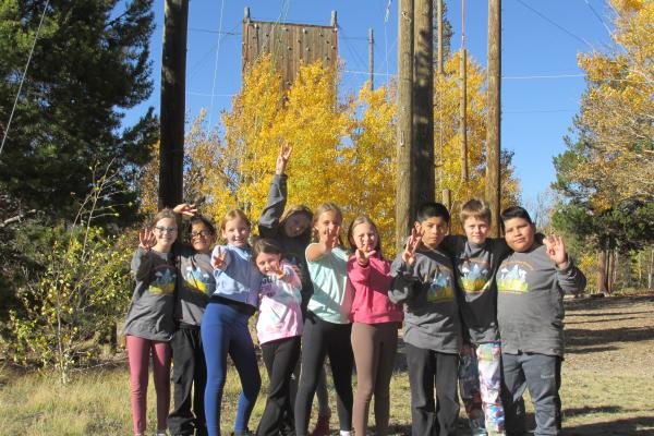 group of students waving and smiling while at ECO week at CSU Mountain Campus on a sunny fall day standing by the ropes course