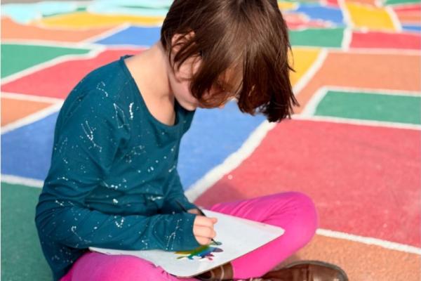 Student sitting cross-legged on the carpet drawing on a paper in her lap.