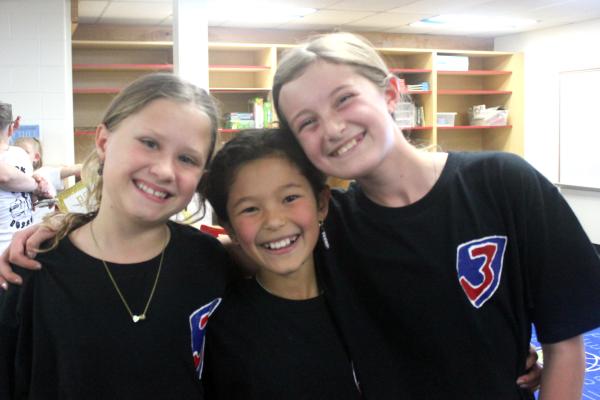 three girls on a battle of the books team with arms around shoulders smiling black t-shirts