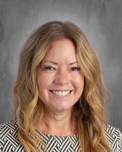 smiling female teacher with  long dark blonde hair in a gray top