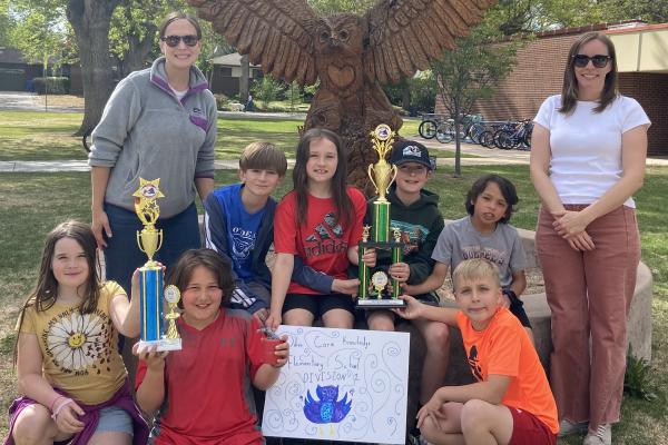 OM team - six boys and a girl grades 3-4 - and mom coaches standing outside by the owl carved tree truck in front of odea