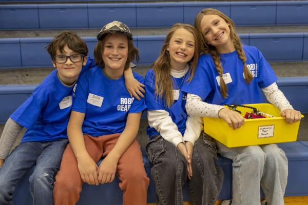 Two girls and two boys from O'Dea's Lego robotics team sitting together smiling during the lego robotics competition at Poudre High School.
