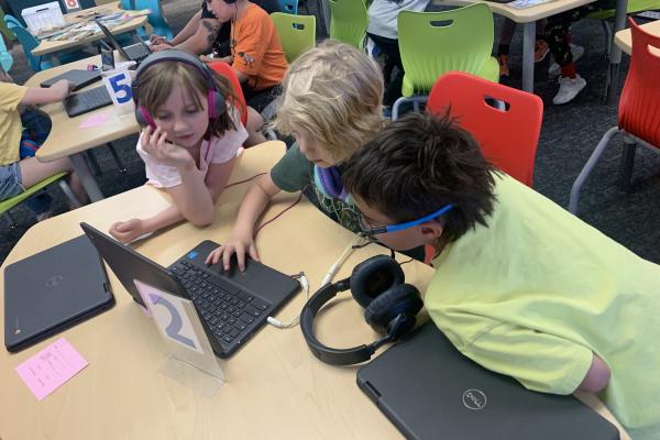 three students wearing headphones - a girl and two boys - working together on code.org